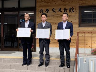 浅原交流会館の前で協定書を手にする市長ほか